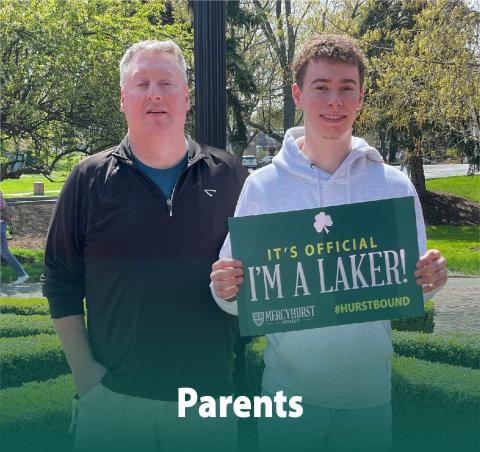 A dad posing with his son who has decided to attend ܼˮ̳. The son holds a poster reading "It's Official. I'm a Laker!"