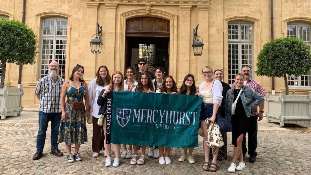 a group of students and professors pose in France with a ܼˮ̳ flag